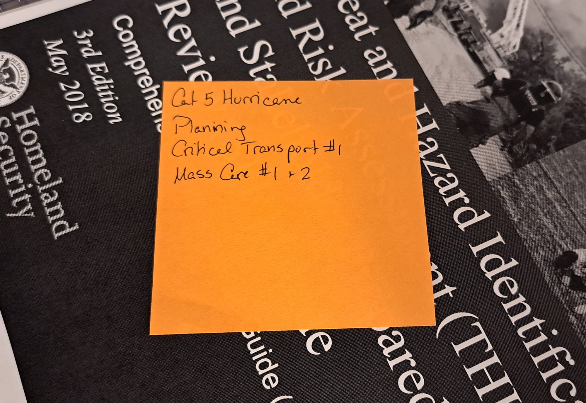 A square orange sticky note with the words "Cat[egory] 5 Hurricane | Planning | Critical Transport #1 | Mass Care #1 & 2", over the FEMA THIRA/SPR Review Guide
